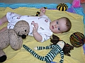 Baby playing with Flopsy Bear and other knitted toys